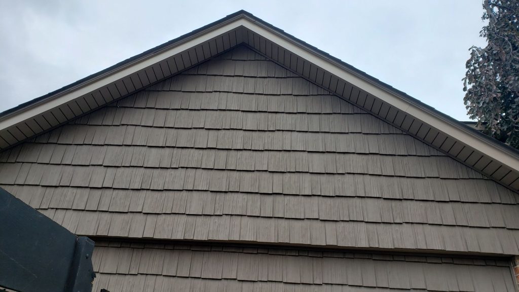 After: the same garage gable covered in taupe-brown shake-style siding with light trim and vented soffit