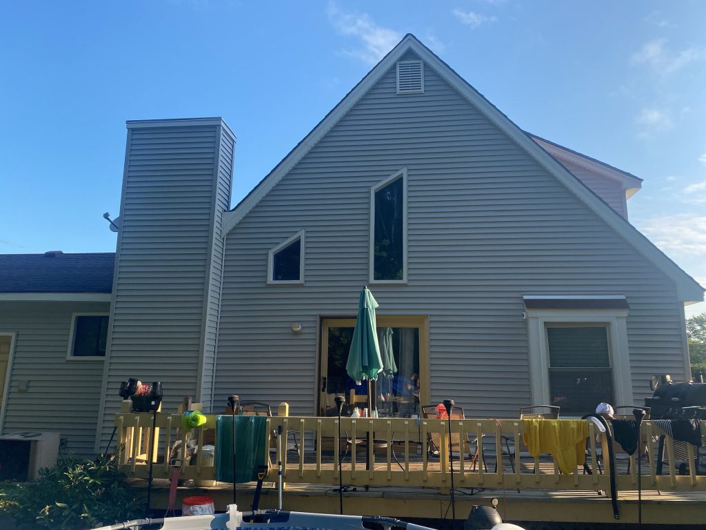 After: the same home with light gray horizontal lap siding on the gable and wrapped chimney chase, white window trim and a louvered gable vent