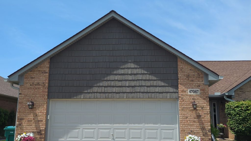 Brick home in Mount Clemens with a charcoal gray shake-style siding gable above a light garage door