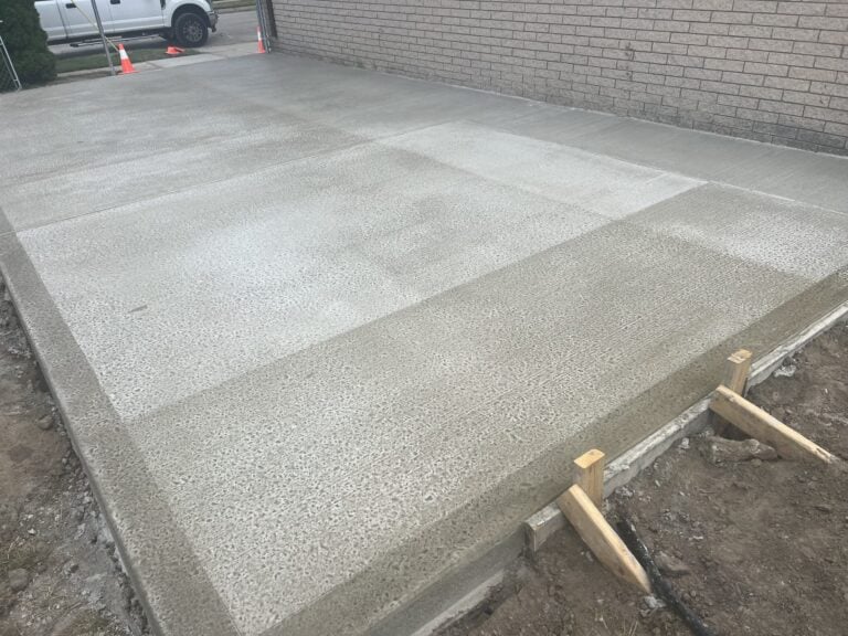 Freshly poured concrete driveway slab with forms still in place beside a brick wall on Cedar Street in St. Clair Shores, MI