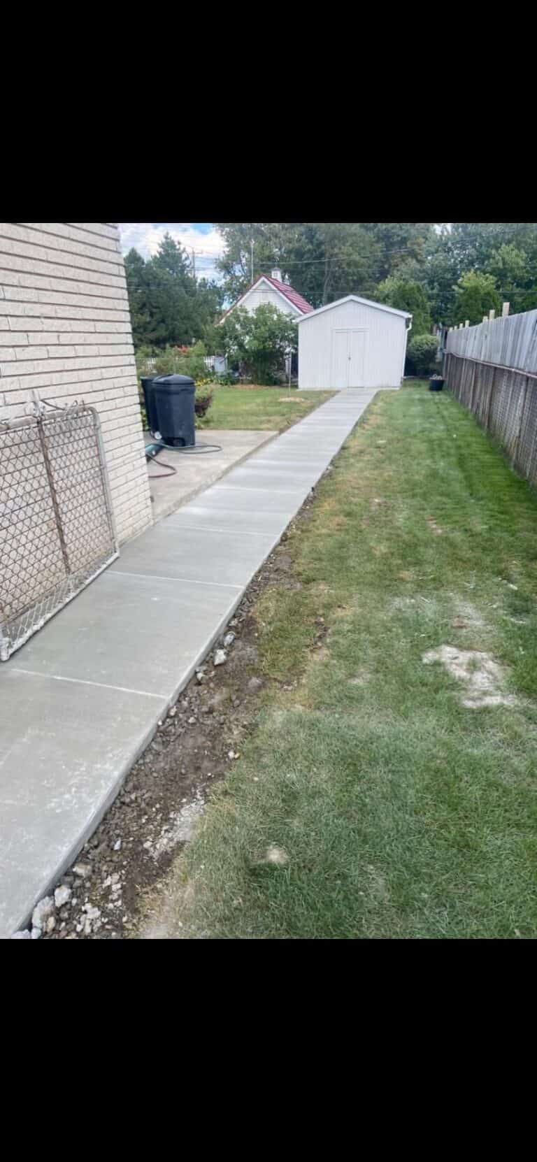 Freshly poured concrete sidewalk along the side of a home toward a backyard shed on Havana Drive in Sterling Heights, MI