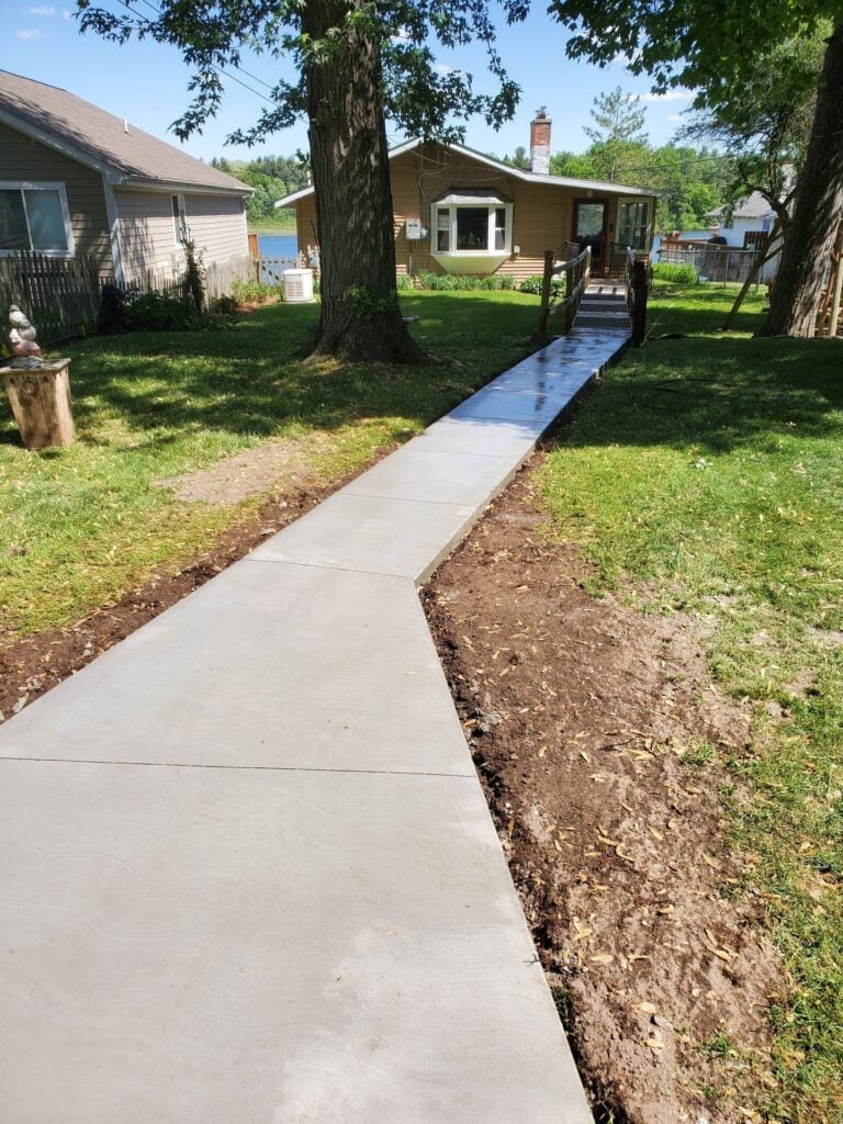 Freshly poured broom-finish concrete walkway leading through a lawn to a lakeside home on Beach Drive in Orion Township, MI