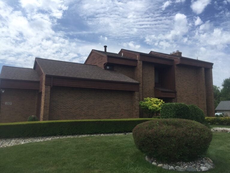Large contemporary brick home with a newly installed roof and rounded shrubs on Aspinwall Street in Troy, MI