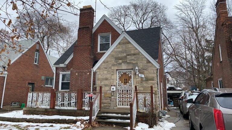 Brick and stone storybook-style home with a new dark shingle roof in winter on Delaware Street in Pontiac, MI