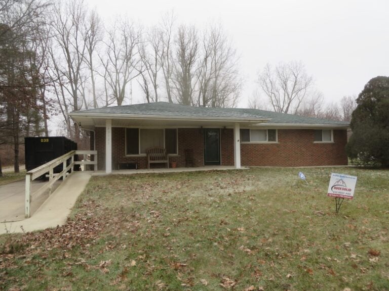 Single-story brick ranch with a new roof and a Rock Solid Exteriors yard sign on Judd Road in Belleville, MI