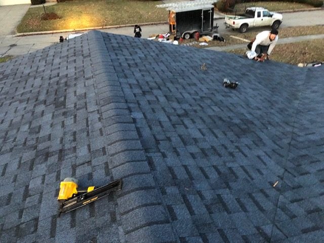 Roofer working on a new blue-gray shingle roof with a nail gun on the ridge on Westland Avenue in Southfield, MI