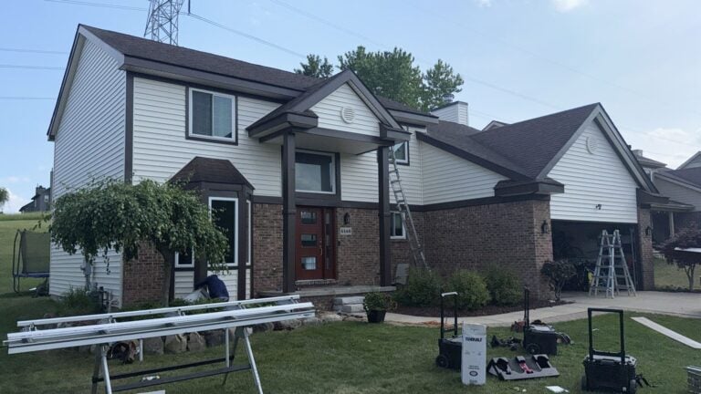 Two-story home with new white siding, dark trim and brick during a siding project on Ancroft Drive in Clarkston, MI
