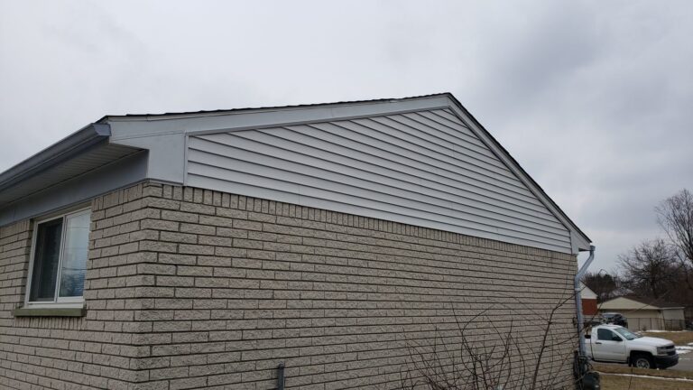 Gable end of a single-story brick home with new light gray lap siding on Burns Street in Inkster, MI