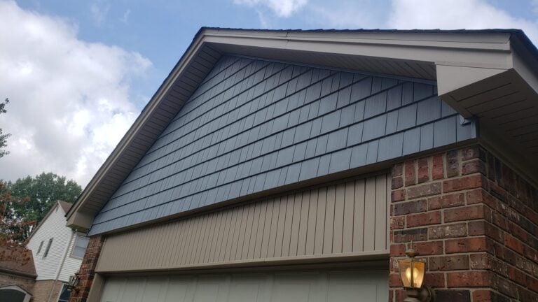 Close-up of a gable with new gray shake-style siding and vertical siding above brick on Oneida Drive in Clinton Township, MI